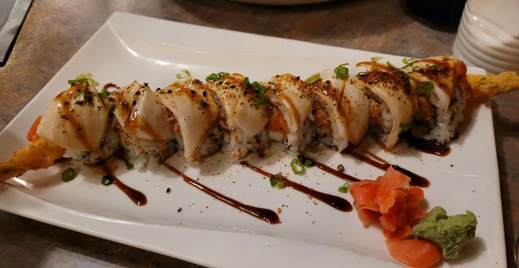 Beautiful sushi roll lays across rectangular plate with ginger and wasabi Family Fest