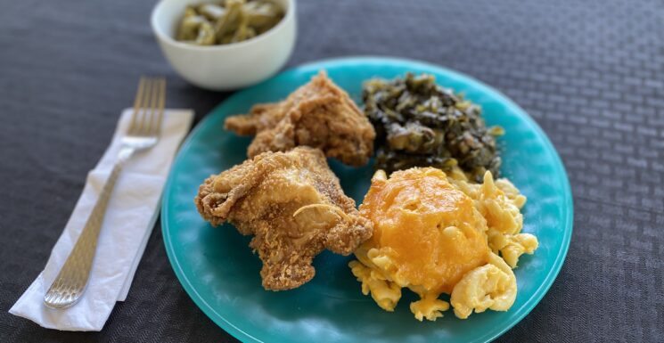 A plate filled with fried chicken, greens, and macaroni and cheese with a side of green beans from Hometown Grill full of Southern and Soul flavor sits ready to eat